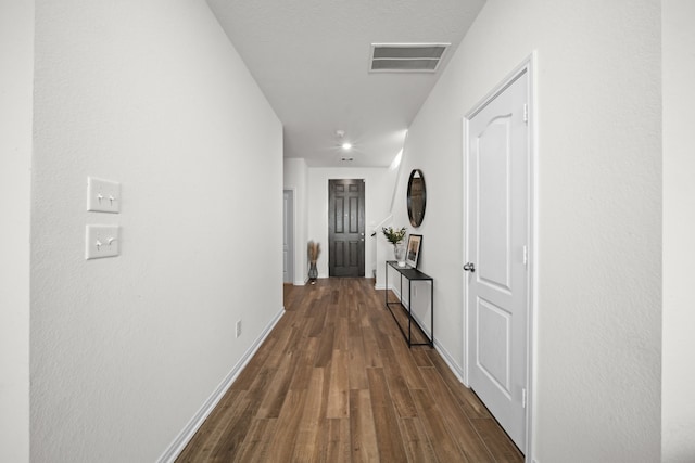 hall featuring visible vents, baseboards, and dark wood finished floors