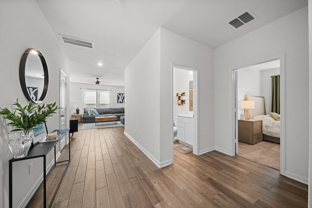 hall with visible vents, baseboards, and wood finished floors