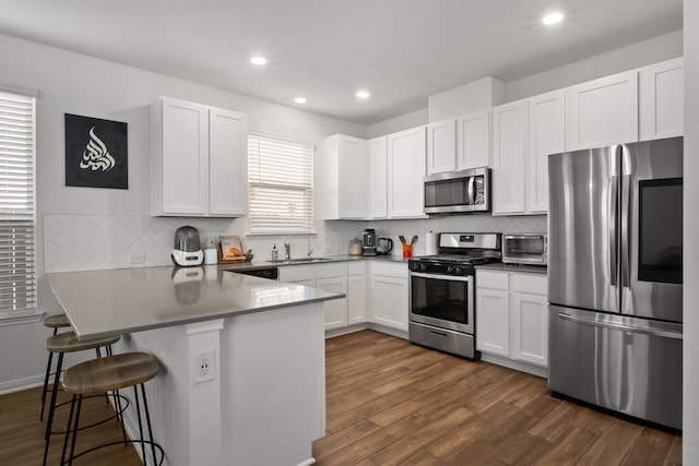 kitchen with dark wood-style floors, white cabinetry, stainless steel appliances, a peninsula, and a breakfast bar area