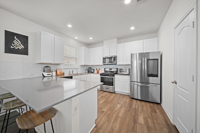 kitchen featuring white cabinetry, a breakfast bar area, a peninsula, stainless steel appliances, and a sink