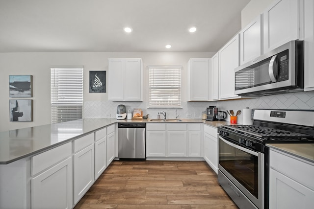 kitchen featuring wood finished floors, a peninsula, stainless steel appliances, white cabinets, and backsplash