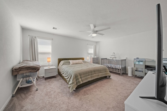 bedroom featuring a textured ceiling, multiple windows, visible vents, and light carpet