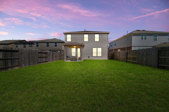 back of house at dusk with a lawn and a fenced backyard