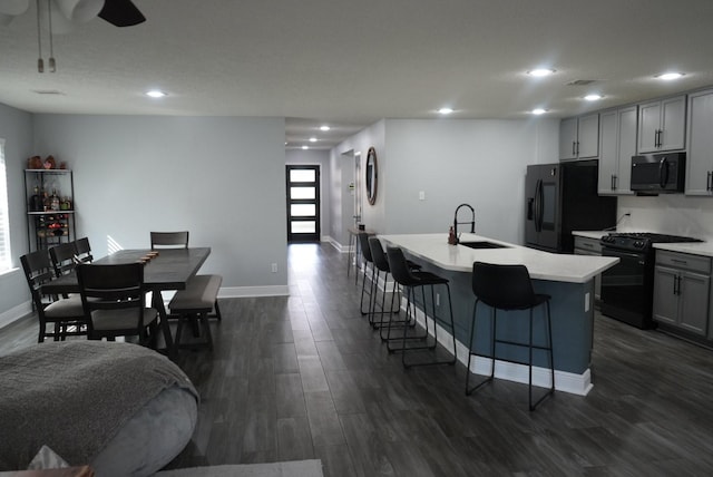 kitchen featuring dark wood-type flooring, an island with sink, a kitchen breakfast bar, black appliances, and a sink