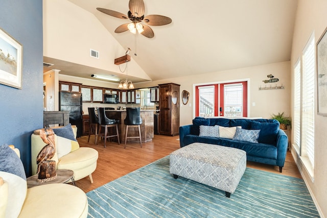 living room featuring light wood finished floors, visible vents, ceiling fan with notable chandelier, and high vaulted ceiling