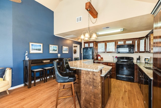 kitchen featuring visible vents, a kitchen island, black appliances, pendant lighting, and light wood-type flooring