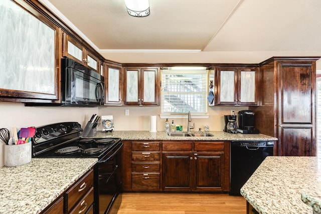 kitchen with light stone countertops, a sink, black appliances, dark brown cabinets, and light wood-type flooring