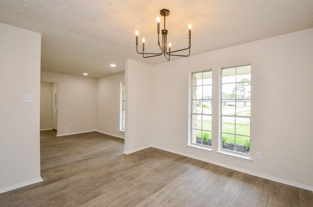 empty room featuring a chandelier, a healthy amount of sunlight, and wood finished floors