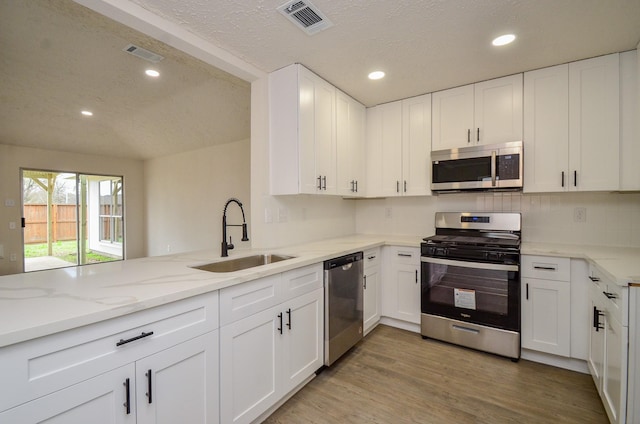 kitchen with visible vents, light stone countertops, light wood-style flooring, stainless steel appliances, and a sink