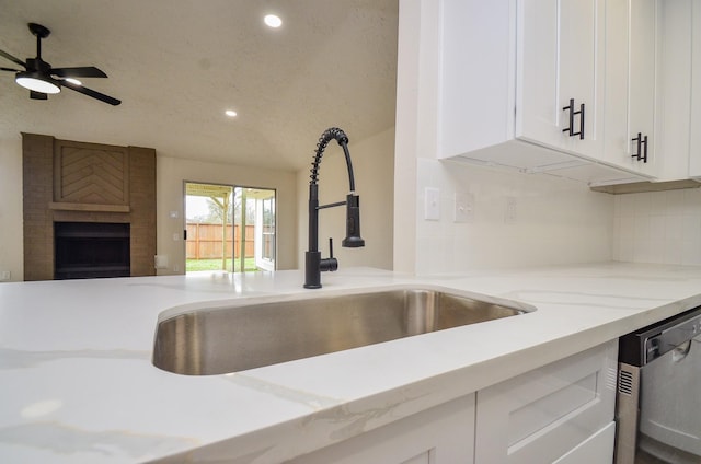 kitchen with a fireplace, a sink, white cabinets, dishwasher, and open floor plan