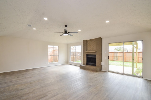 unfurnished living room featuring visible vents, plenty of natural light, a brick fireplace, and a textured ceiling