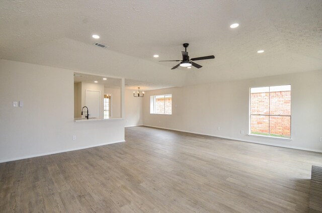 unfurnished living room featuring ceiling fan with notable chandelier, a textured ceiling, baseboards, and wood finished floors