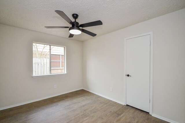 spare room with ceiling fan, wood finished floors, baseboards, and a textured ceiling