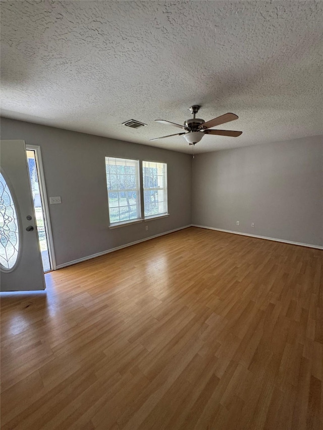 interior space with a ceiling fan, baseboards, visible vents, a textured ceiling, and light wood-type flooring