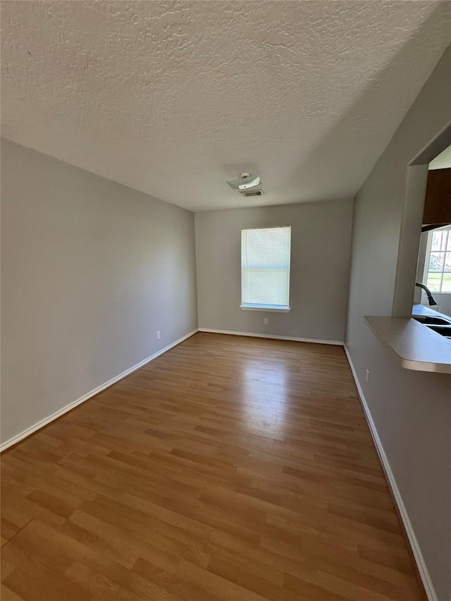 empty room with light wood finished floors, visible vents, a textured ceiling, and baseboards