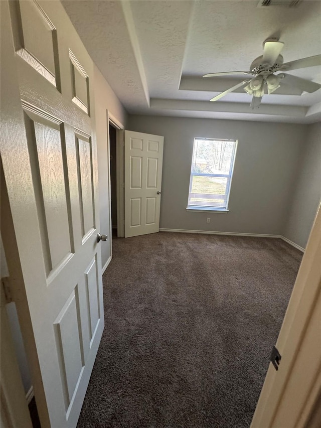 unfurnished bedroom with visible vents, a raised ceiling, a textured ceiling, dark colored carpet, and baseboards