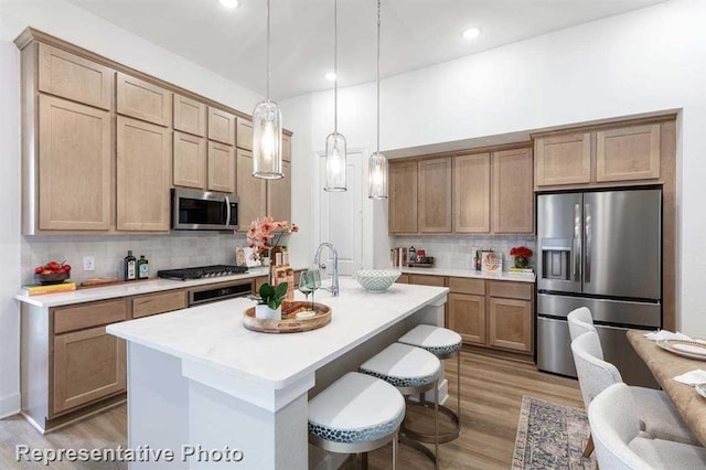 kitchen with tasteful backsplash, light countertops, appliances with stainless steel finishes, light wood-style floors, and hanging light fixtures