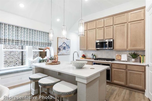 kitchen with tasteful backsplash, light countertops, an island with sink, appliances with stainless steel finishes, and light wood-style floors