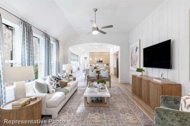 living area featuring ceiling fan, arched walkways, light wood-style flooring, and vaulted ceiling