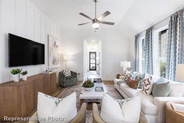 living area with arched walkways, vaulted ceiling, ceiling fan, and wood finished floors