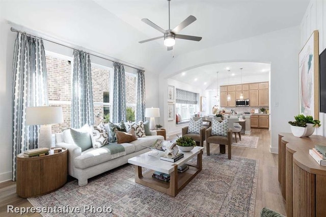 living area featuring light wood finished floors, ceiling fan, baseboards, lofted ceiling, and arched walkways