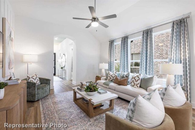 living area with baseboards, lofted ceiling, wood finished floors, arched walkways, and a ceiling fan