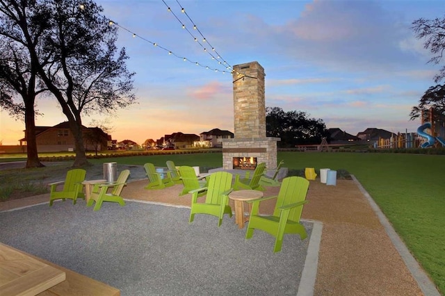 view of playground with a lawn, a warm lit fireplace, and a patio area