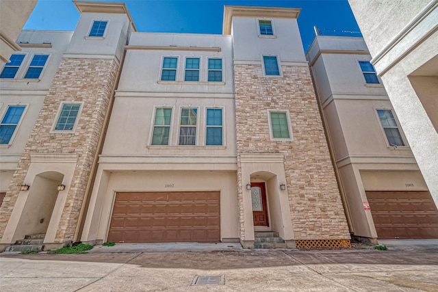 townhome / multi-family property with stone siding, stucco siding, driveway, and an attached garage