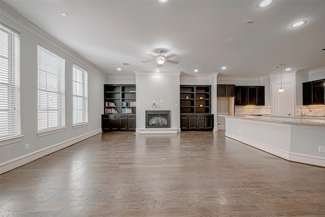 unfurnished living room featuring a fireplace with raised hearth, a ceiling fan, ornamental molding, recessed lighting, and baseboards