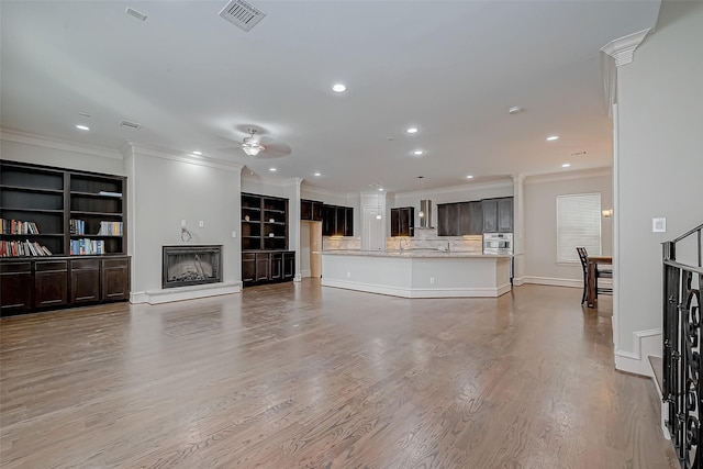 living room featuring visible vents, a fireplace with raised hearth, light wood-type flooring, ornamental molding, and a ceiling fan