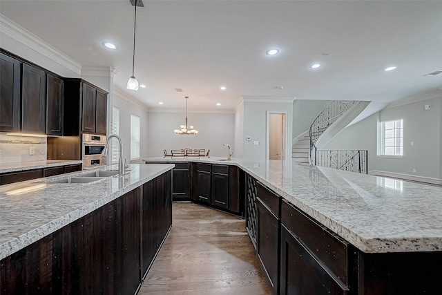 kitchen featuring light wood finished floors, backsplash, crown molding, a notable chandelier, and a sink