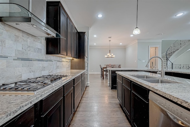 kitchen featuring wall chimney range hood, light wood-type flooring, ornamental molding, appliances with stainless steel finishes, and a sink