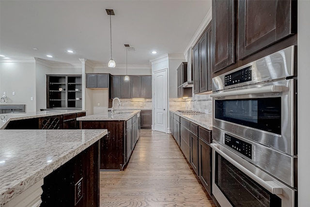 kitchen with an island with sink, a sink, dark brown cabinets, light wood-style floors, and appliances with stainless steel finishes