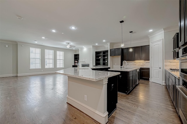 kitchen featuring crown molding, open floor plan, wood finished floors, and a center island with sink