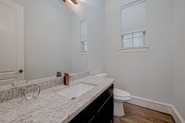 bathroom featuring vanity, wood finished floors, baseboards, toilet, and a wealth of natural light