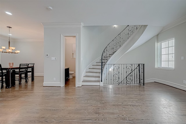 living area featuring a notable chandelier, ornamental molding, wood finished floors, baseboards, and stairs
