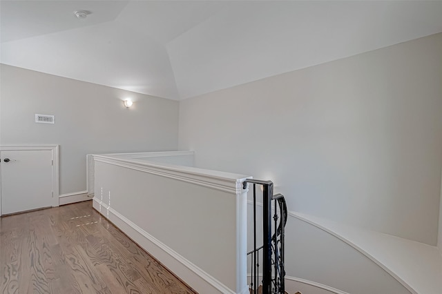 corridor with an upstairs landing, visible vents, lofted ceiling, and wood finished floors