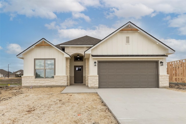 view of front facade with stone siding, driveway, roof with shingles, and an attached garage