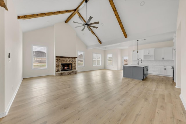 unfurnished living room featuring a brick fireplace, ceiling fan, beam ceiling, light wood-style flooring, and high vaulted ceiling