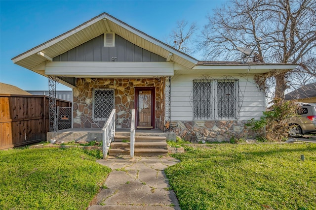 view of front of home with a front yard, fence, a porch, stone siding, and board and batten siding