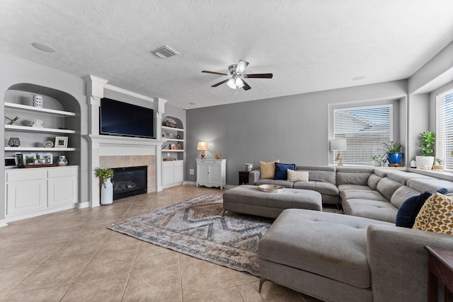 living area with built in shelves, visible vents, light tile patterned flooring, a textured ceiling, and a tiled fireplace