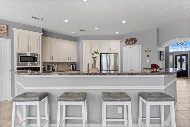 kitchen featuring a breakfast bar, dark stone countertops, visible vents, and stainless steel appliances