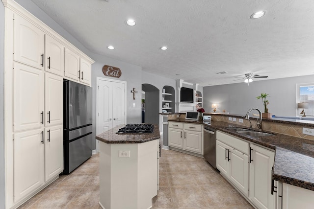 kitchen with a sink, a kitchen island, stainless steel appliances, arched walkways, and dark stone counters