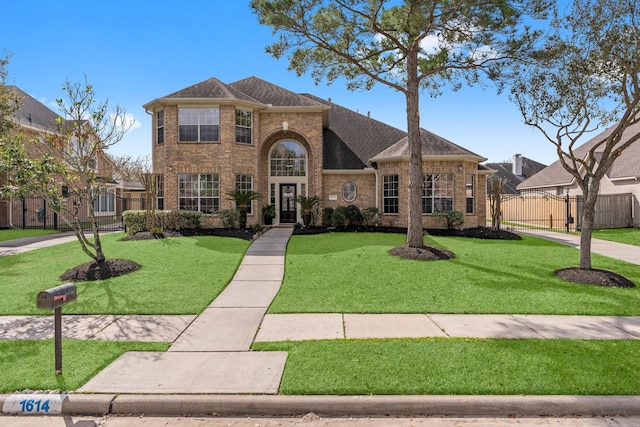 traditional home featuring a front yard, a gate, fence, a shingled roof, and brick siding