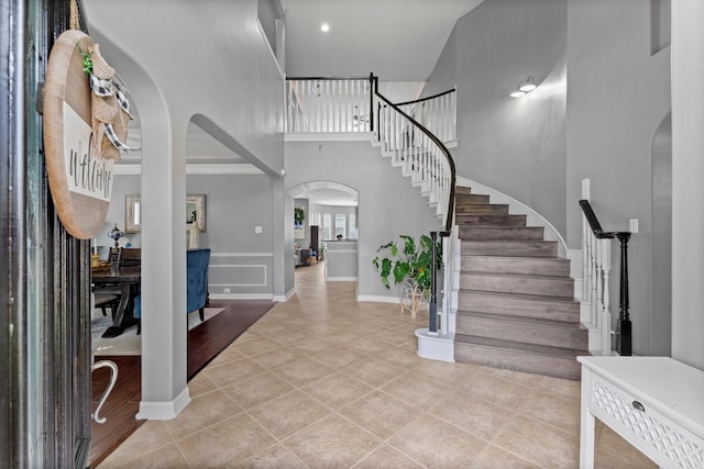 tiled foyer featuring arched walkways, a towering ceiling, and stairs