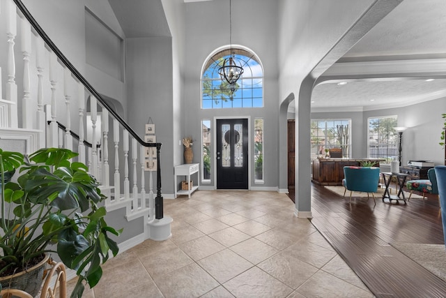 tiled entrance foyer with stairs, an inviting chandelier, baseboards, and arched walkways