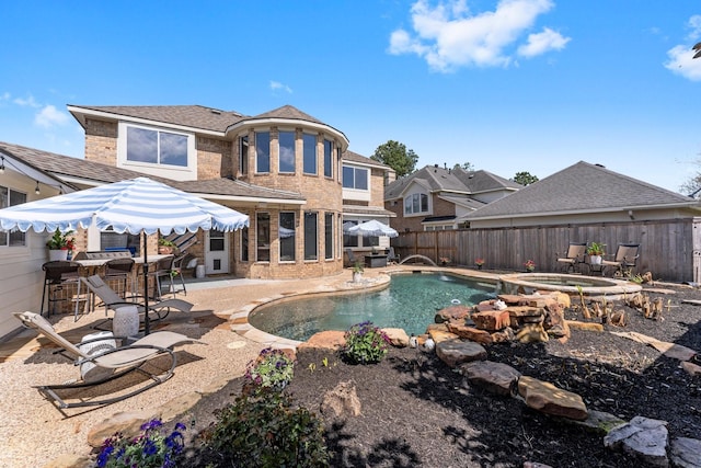 rear view of house featuring a patio area, a pool with connected hot tub, brick siding, and a fenced backyard