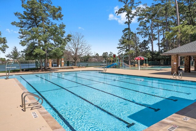 pool with a patio, fence, playground community, and a water slide