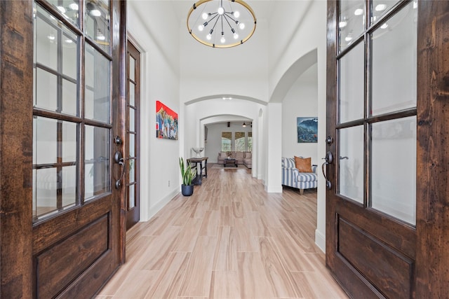 foyer with baseboards, light wood-type flooring, an inviting chandelier, a towering ceiling, and arched walkways