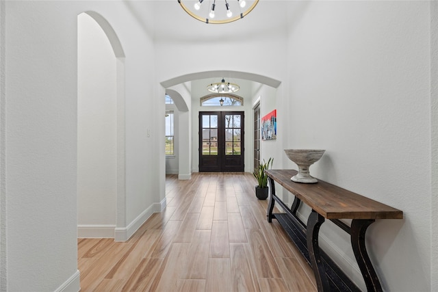 foyer with a notable chandelier, arched walkways, light wood-style floors, and french doors